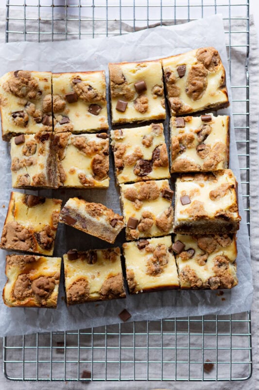 A top down shot of the 16 squares of cheesecake cookie bars on a wire rack