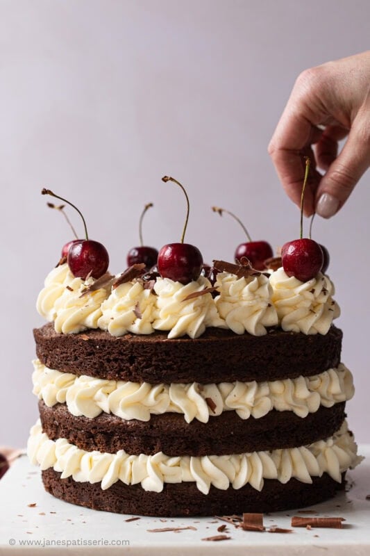 A hand placing fresh cherries on a black forest fudge cake