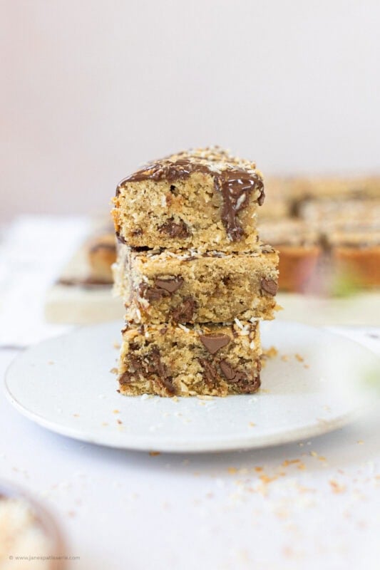 Three Coconut Chocolate Blondies stacked on a plate
