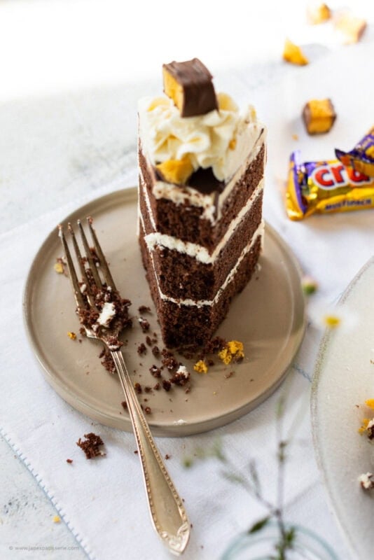 A slice of crunchie drip cake on a plate with a fork