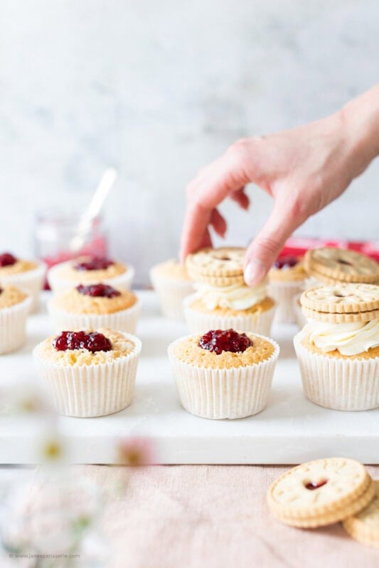 A hand decorating a Jammie Dodger cupcake