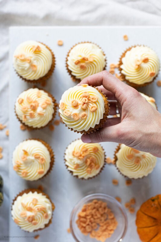 A hand holding a pumpkin cupcake with cream cheese frosting
