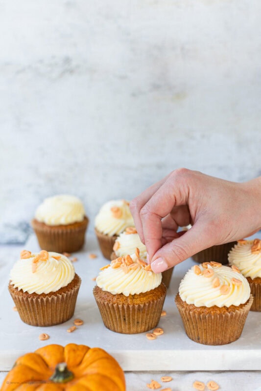 A hand placing a final decoration on a pumpkin cupcake