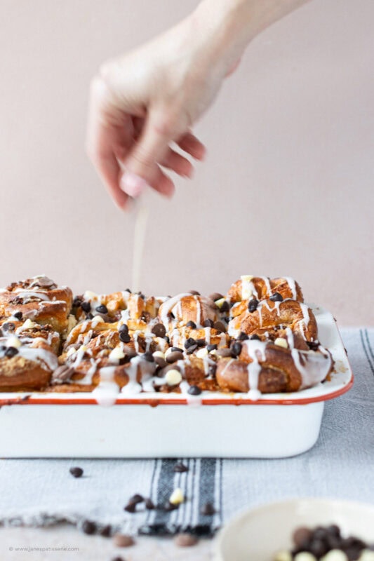 A hand decoratig a tray of Sticky Chocolate Sweet Rolls