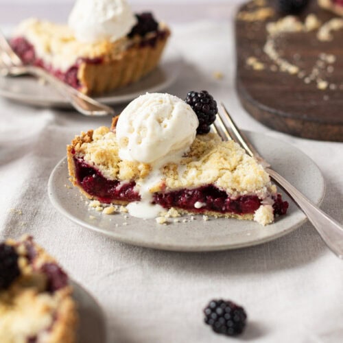 Close up of Apple and Blackberry Crumble Pie on a plate with ice cream and a fork