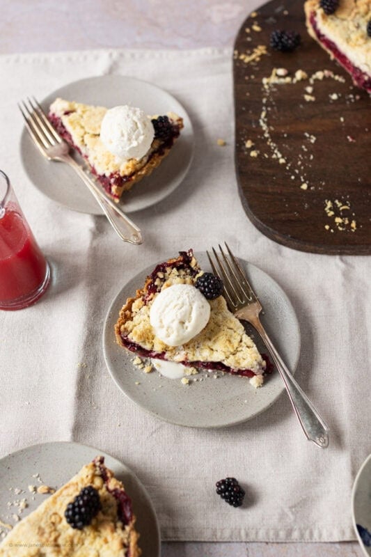 A slice of Apple and Blackberry Crumble Pie on a plate with ice cream