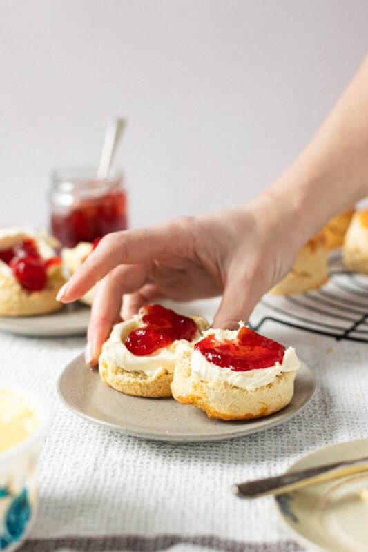 A hand going to take a classic buttery scone from a plate