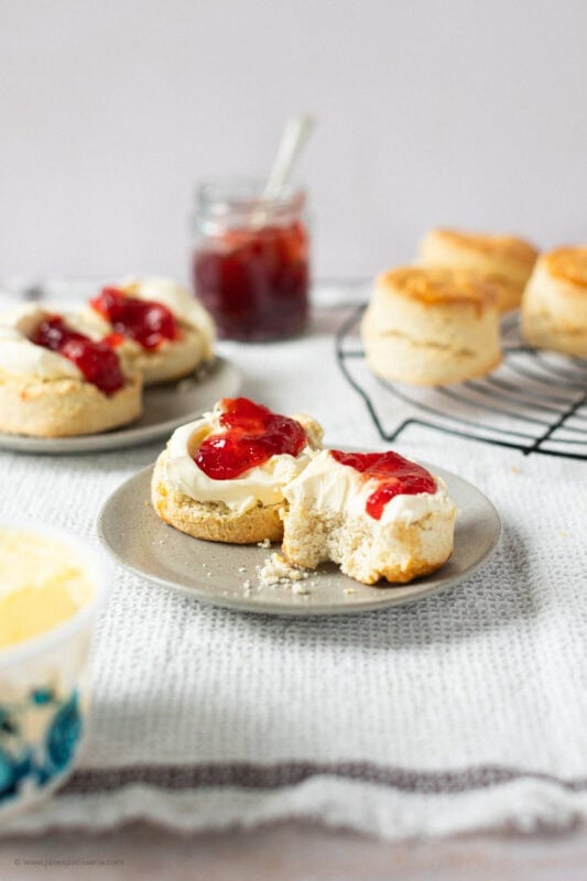 Two classic buttery scones on a plate with a bite taken from one