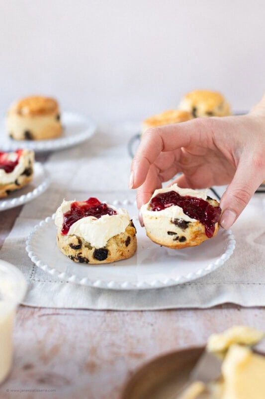 A hand taking a Fruit scone from a plate
