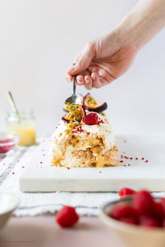 A hand decorating the lemon meringue roulade with a spoon