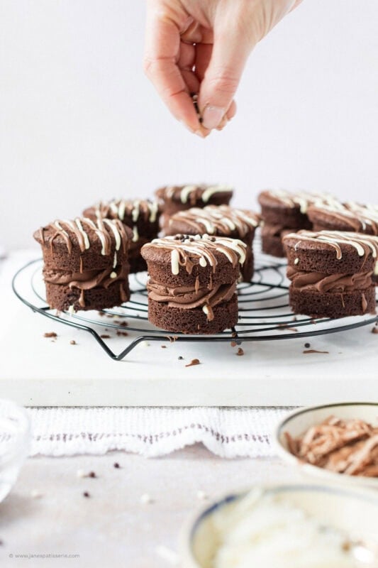 A hand decorating Mini Chocolate Cakes on a wire rack
