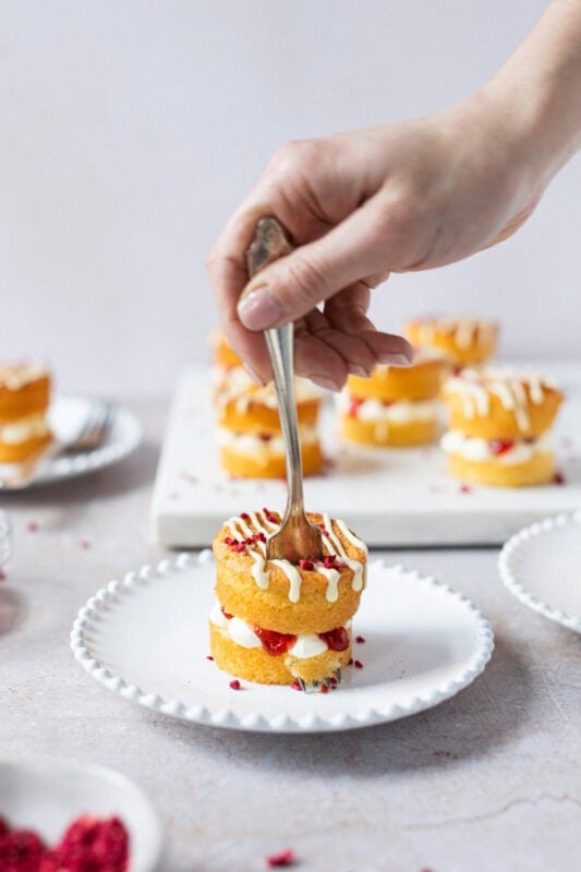 A hand and fork cutting into a mini Victoria sponge cake