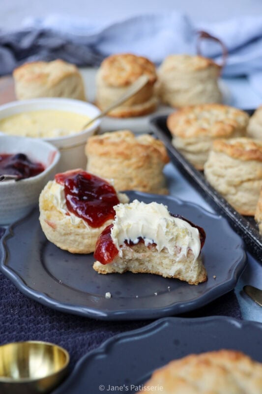 A slathered buttermilk scone with a jam and clotted cream on a plate