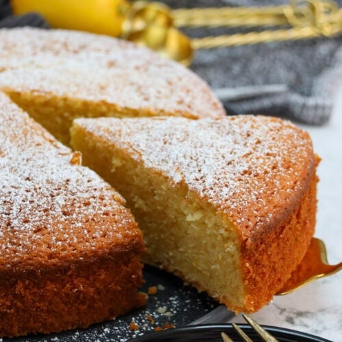 A whole Lemon Olive Oil Cake with a slice being taken