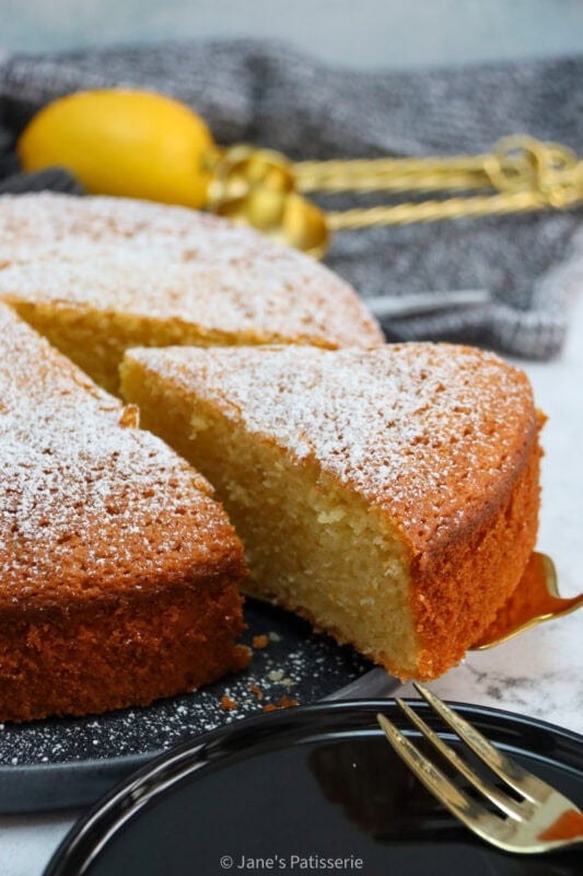 A slice of Lemon Olive Oil Cake being taken from a whole cake