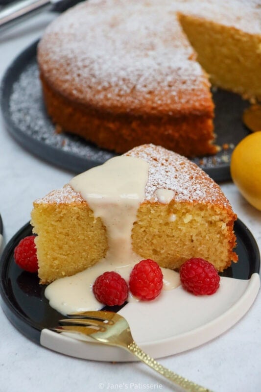 A slice of Lemon Olive Oil Cake on a plate with cream and fresh raspberries.